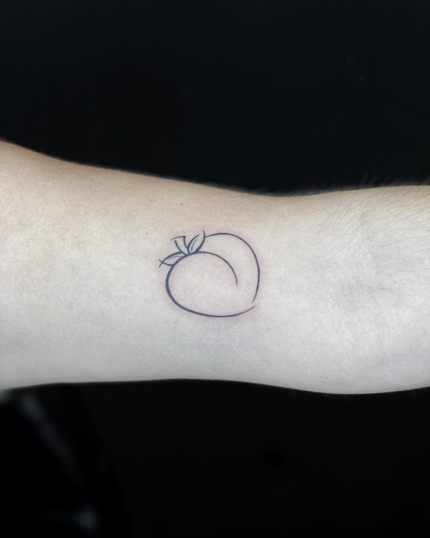 Minimalist peach tattoo outline on a forearm